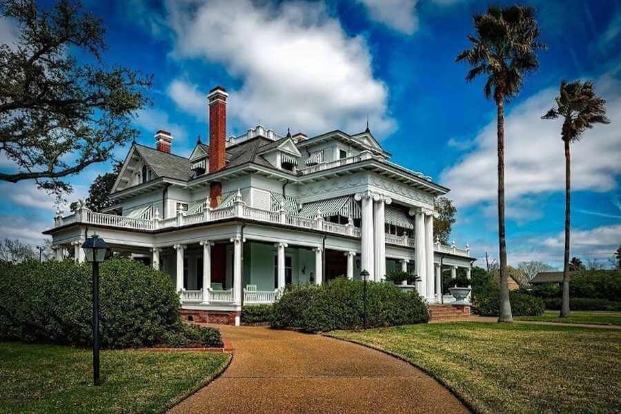 large double-storey house with balconies on both levels surrounded by palm trees and manicured garden