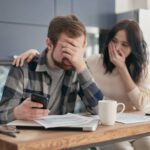 man covering his face in frustration checking expenses and debts with partner comforting him